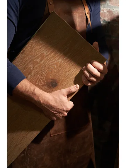 Man holding a sample of hardwood flooring with visible wood grain and natural color